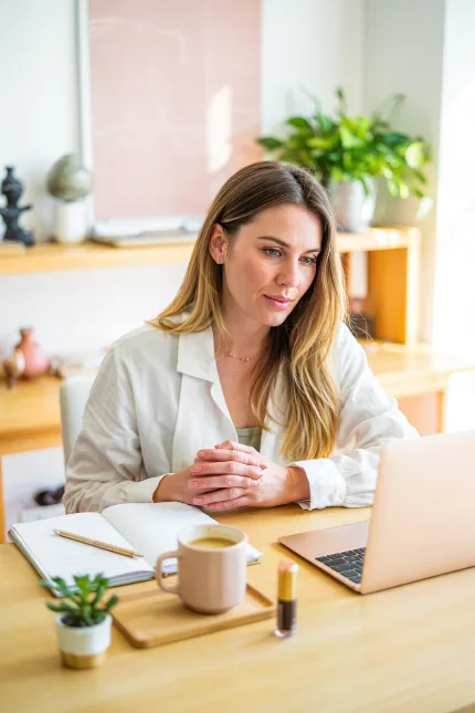 Femme indépendante heureuse devant son agenda et son ordinateur — ambiance bureau féminin lumineux, tons chauds rose et crème